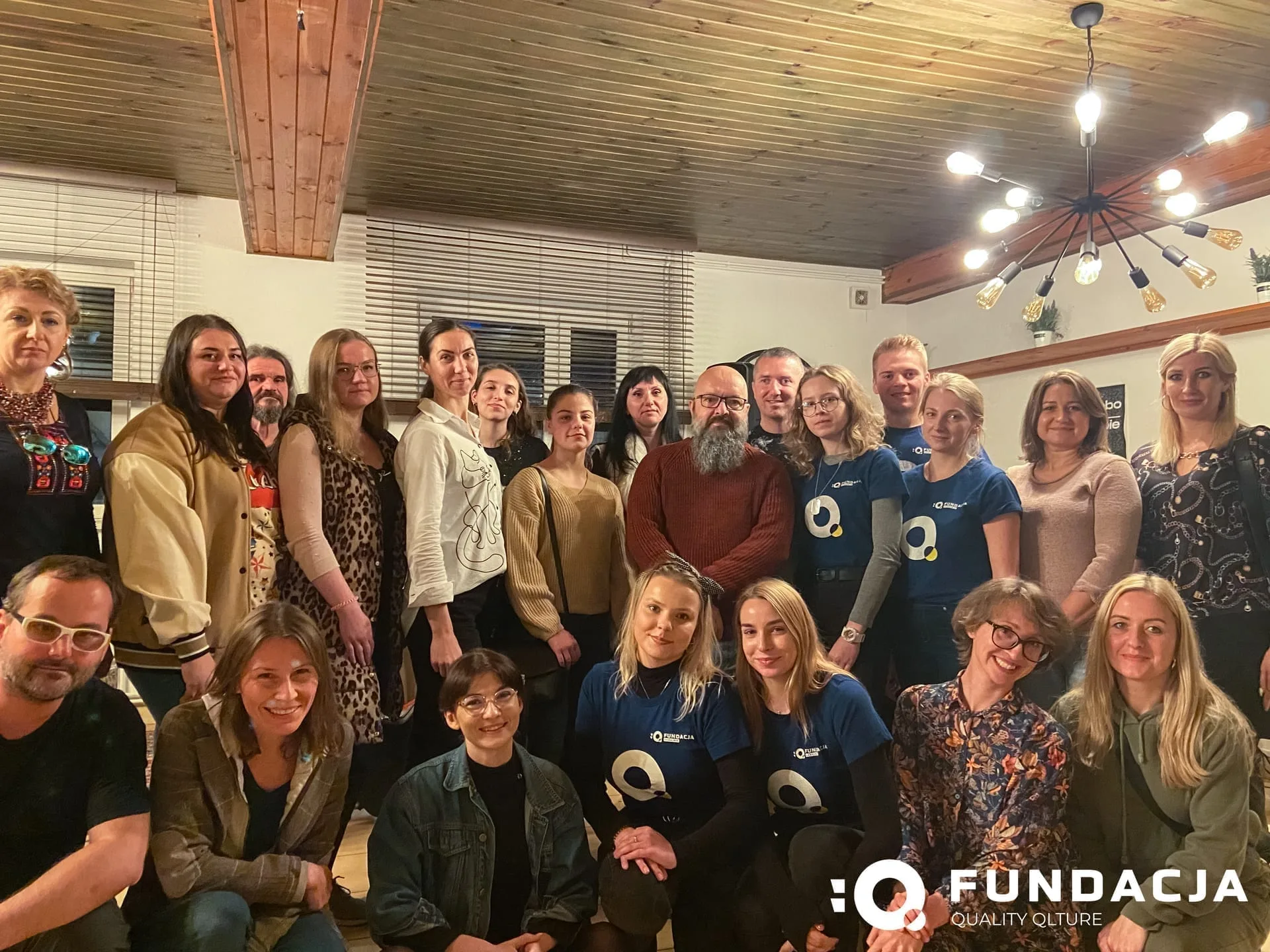 Zespół Fundacji Q — grupowe zdjęcie członków i współpracowników fundacji w pomieszczeniu z drewnianym sufitem.
